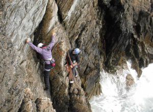 A lead climber is belaying his second on Symphony Crack cliff just above the sea line